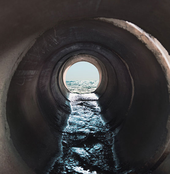 Looking through a large water pipe flowing out to a body of water.